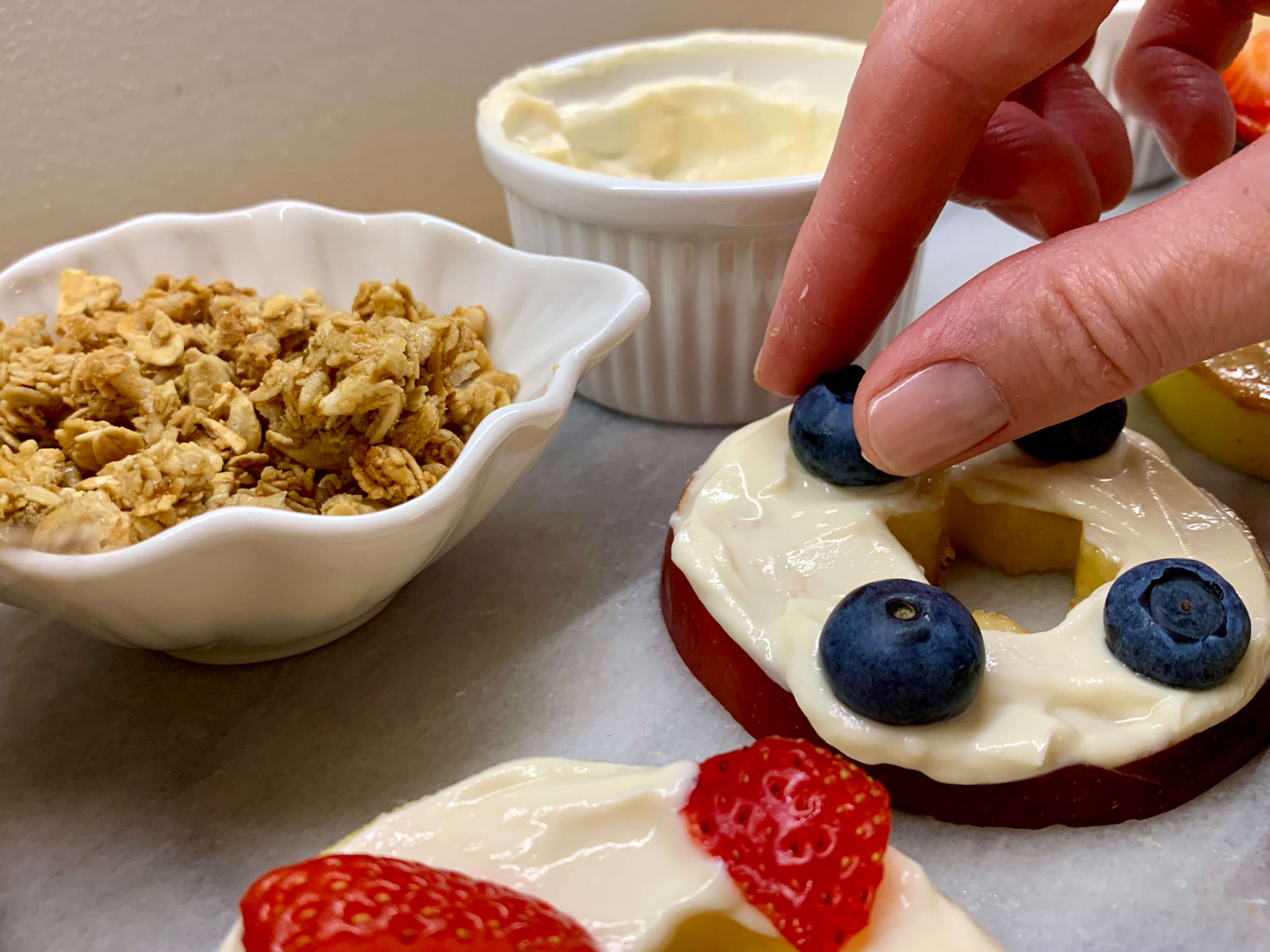 mani che decorano con mirtilli e fragole delle fette di mela con formaggio cremoso