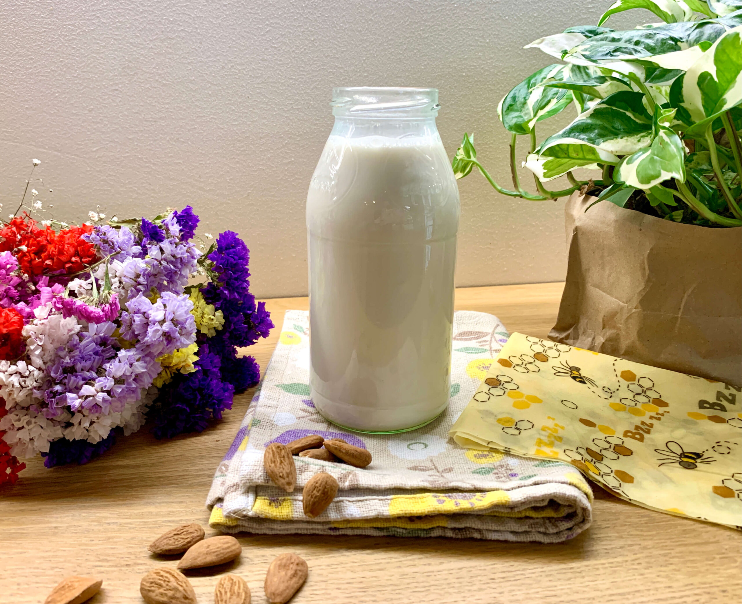 bottiglia di latte con mandorle, fiori e piante attorno