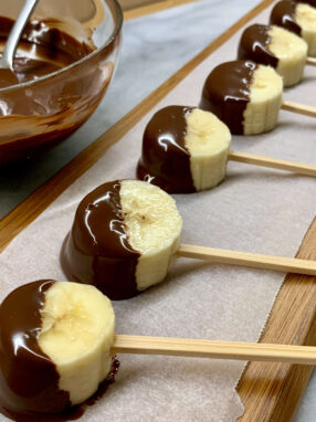 lecca lecca di banana al cioccolato su tagliere di legno con cioccolato fuso a fianco
