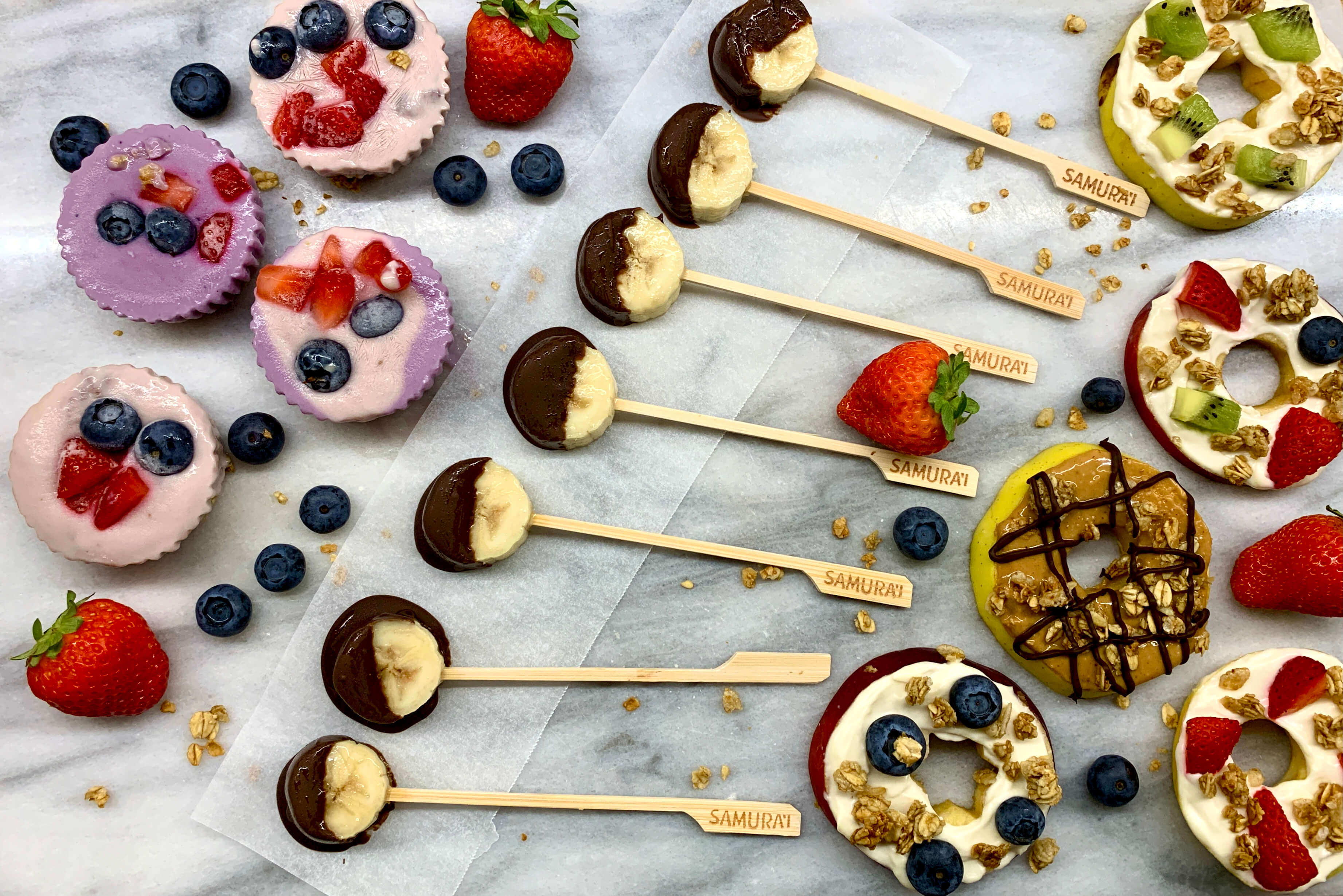 cupcakes di granola con frozen yogurt lecca lecca di banana ricoperti di cioccolato e girelle di mela decorate tutto su un tagliere di marmo
